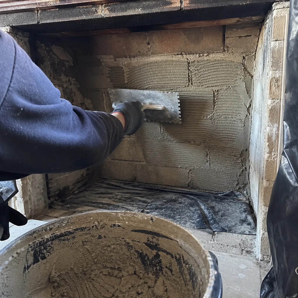 Professional contractor applying mortar to a brick fireplace with a trowel